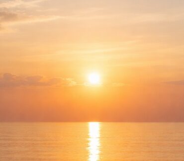Peaceful sunrise over a calm ocean horizon with soft golden light reflecting on still water, symbolizing tranquility and simplicity in cremation services Queens, NY