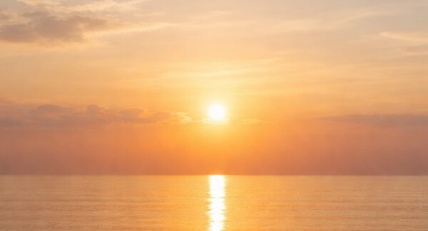 Peaceful sunrise over a calm ocean horizon with soft golden light reflecting on still water, symbolizing tranquility and simplicity in cremation services Queens, NY