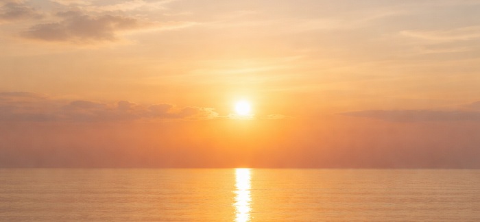 Peaceful sunrise over a calm ocean horizon with soft golden light reflecting on still water, symbolizing tranquility and simplicity in cremation services Queens, NY